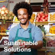 Man in green apron at produce market with fruits and vegetables in the background, promoting sustainable agriculture solutions. - The text in the image reads: Sustainable Solutions. Man in green apron at produce market with fruits and vegetables in the background, promoting sustainable agriculture solutions. - The text in the image reads: Sustainable Solutions.